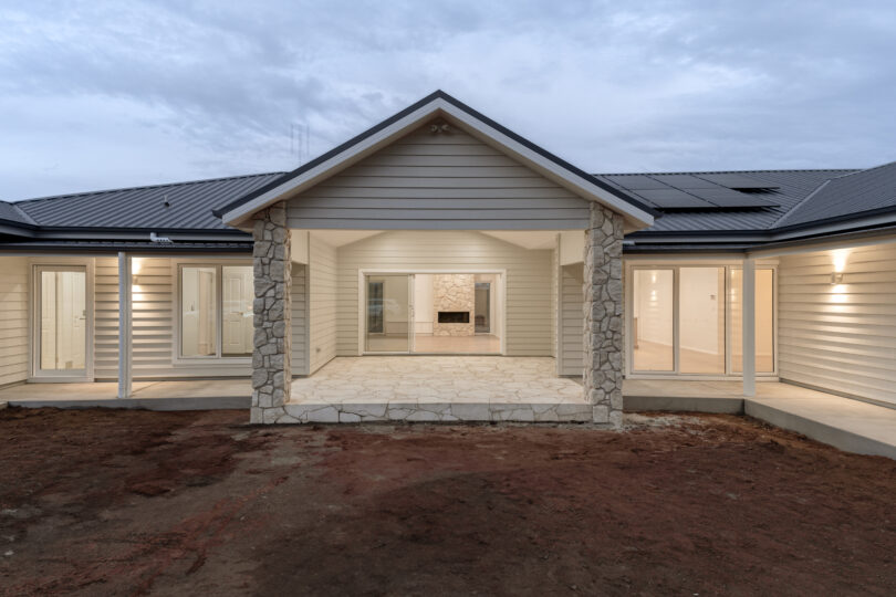 Closer look at the alfresco pavilion—pitched roof, chunky limestone posts and flagstone paving—opening to a living room with stone fireplace, flanked by glazed doors along the veranda.